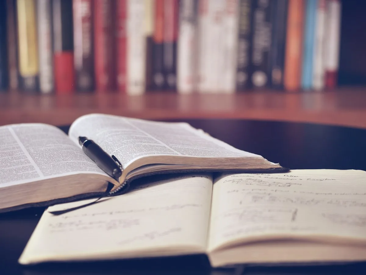 Tumpukan buku dan buku catatan di samping laptop
